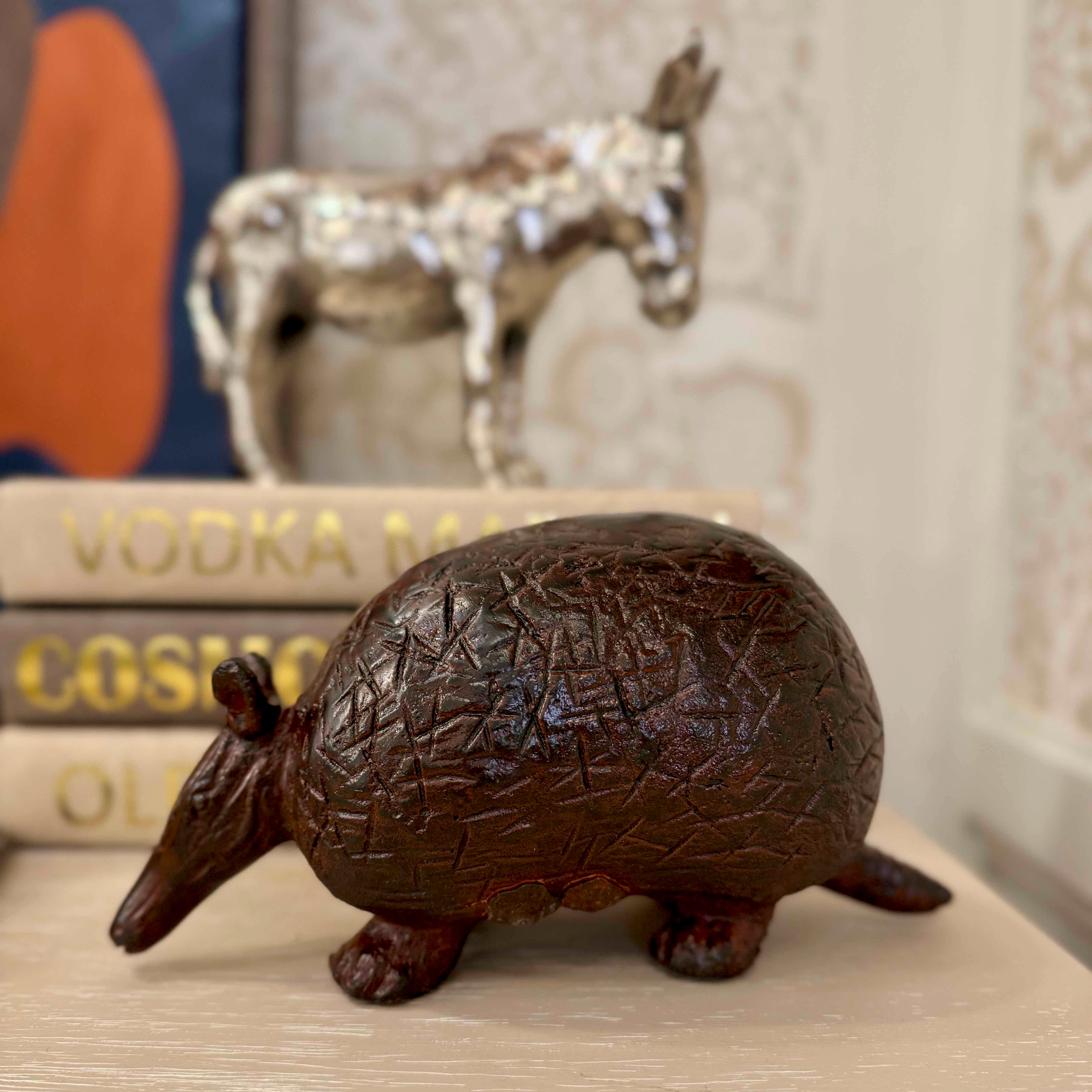 Bronze armadillo figurine on a surface with books and a decorative horse in the background.