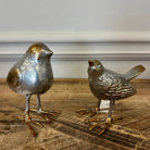 Two metallic bird figurines on a wooden surface with a neutral background