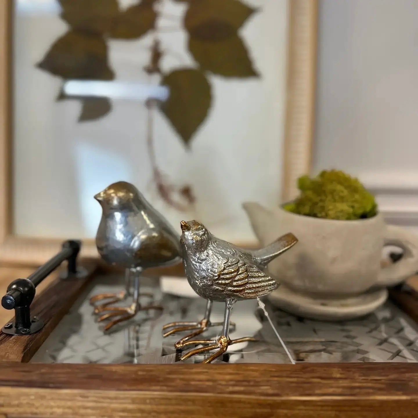 Two metallic bird figurines on a reflective surface with a blurred background