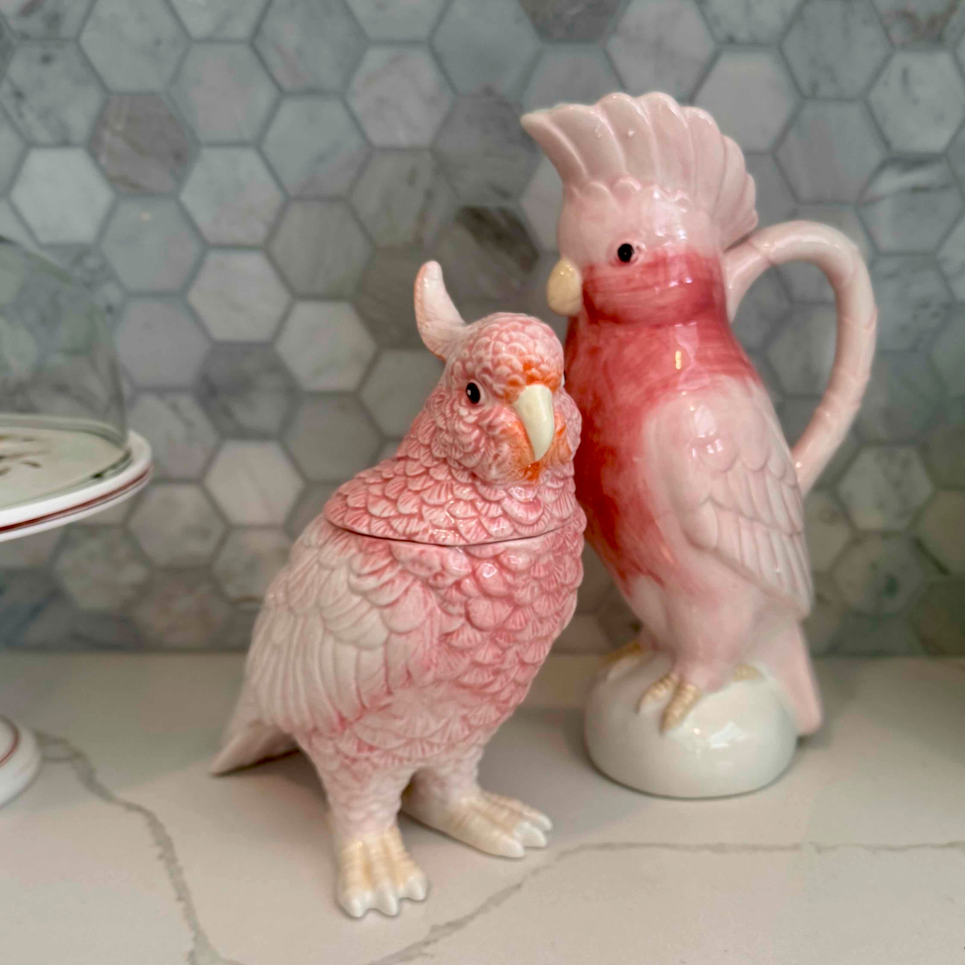 Pink ceramic parrot-shaped jar and lid on a tiled surface with a marble hexagonal tile backsplash.