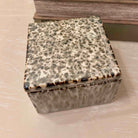 Square decorative box with speckled pattern on a neutral background
