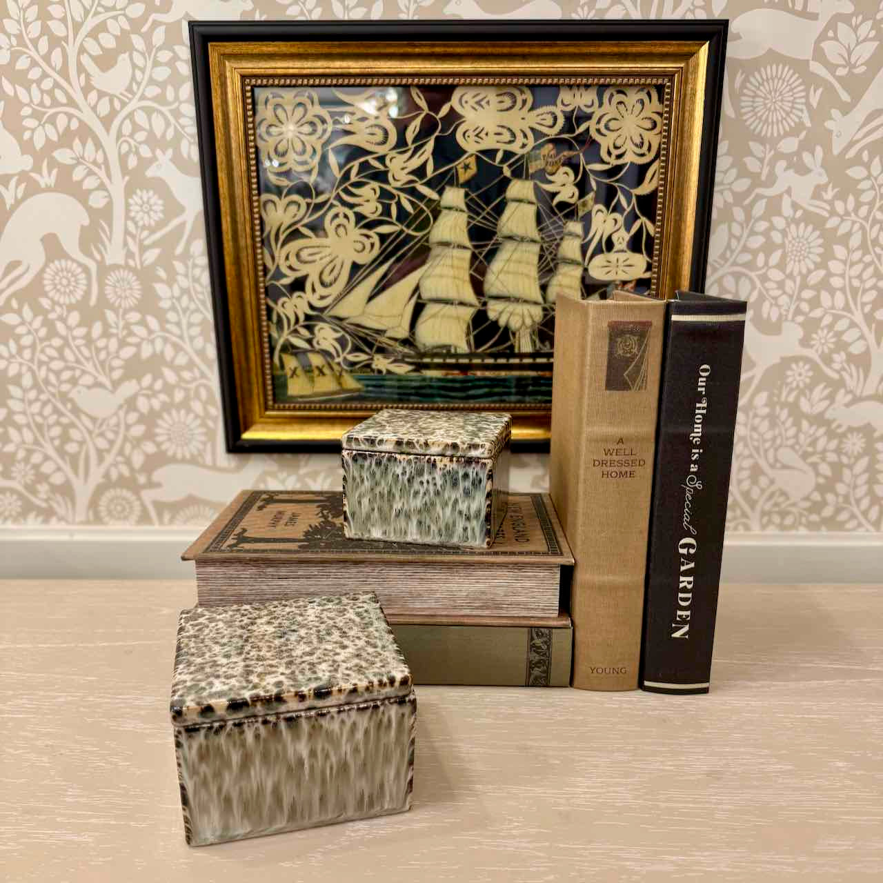 Decorative arrangement with books and a framed picture on a patterned wall.