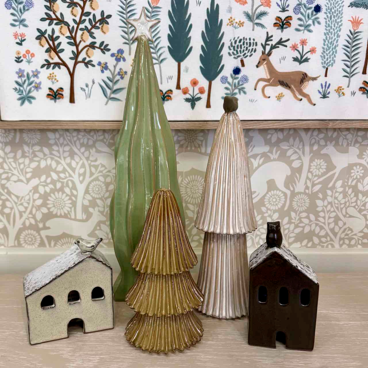 Decorative ceramic trees and houses on a surface with a patterned wallpaper background