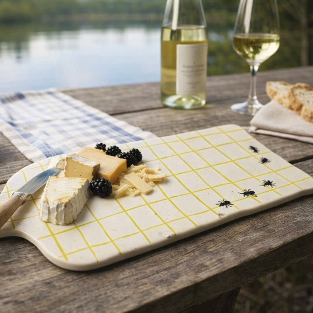 Cheeseboard with assorted cheeses and blackberries on a wooden table by a lake.