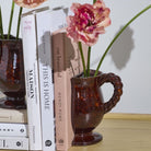 Decorative setup with books and a vase containing pink flowers on a wooden surface.