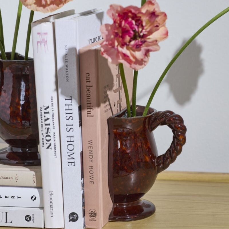 Decorative setup with books and a vase containing pink flowers on a wooden surface.