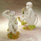 Two ceramic monkey figurines on a decorative base with a soft pink background