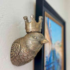 Bronze bird figurine with a crown on a white wall