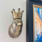 Bronze duck-shaped object with a crown on a white wall next to a framed picture.