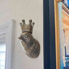 Decorative wall piece with a bird head and crown on a white wall.
