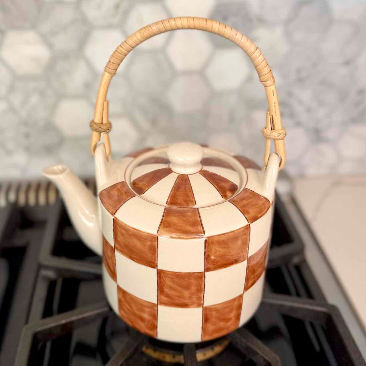 Checkered ceramic teapot with wicker handle on a stove