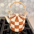 Checkered ceramic teapot with wicker handle on a stove