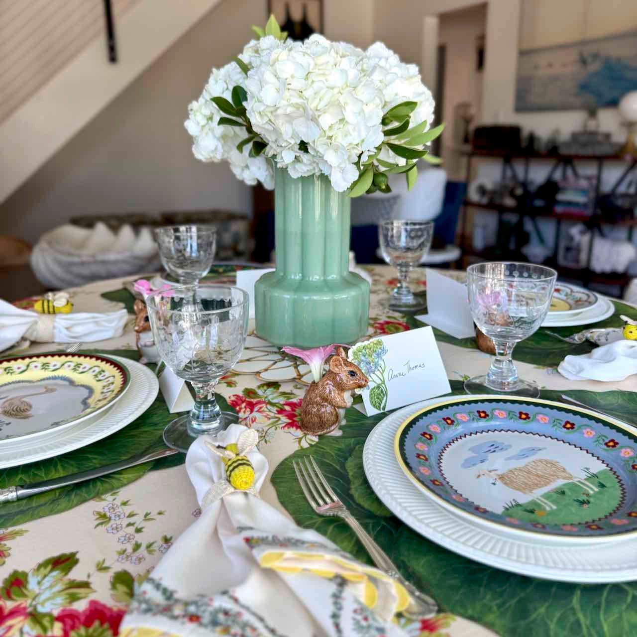 Easter-themed table setting with floral centerpiece, plates, and glasses.