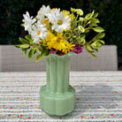 Green vase with flowers on a patterned tablecloth
