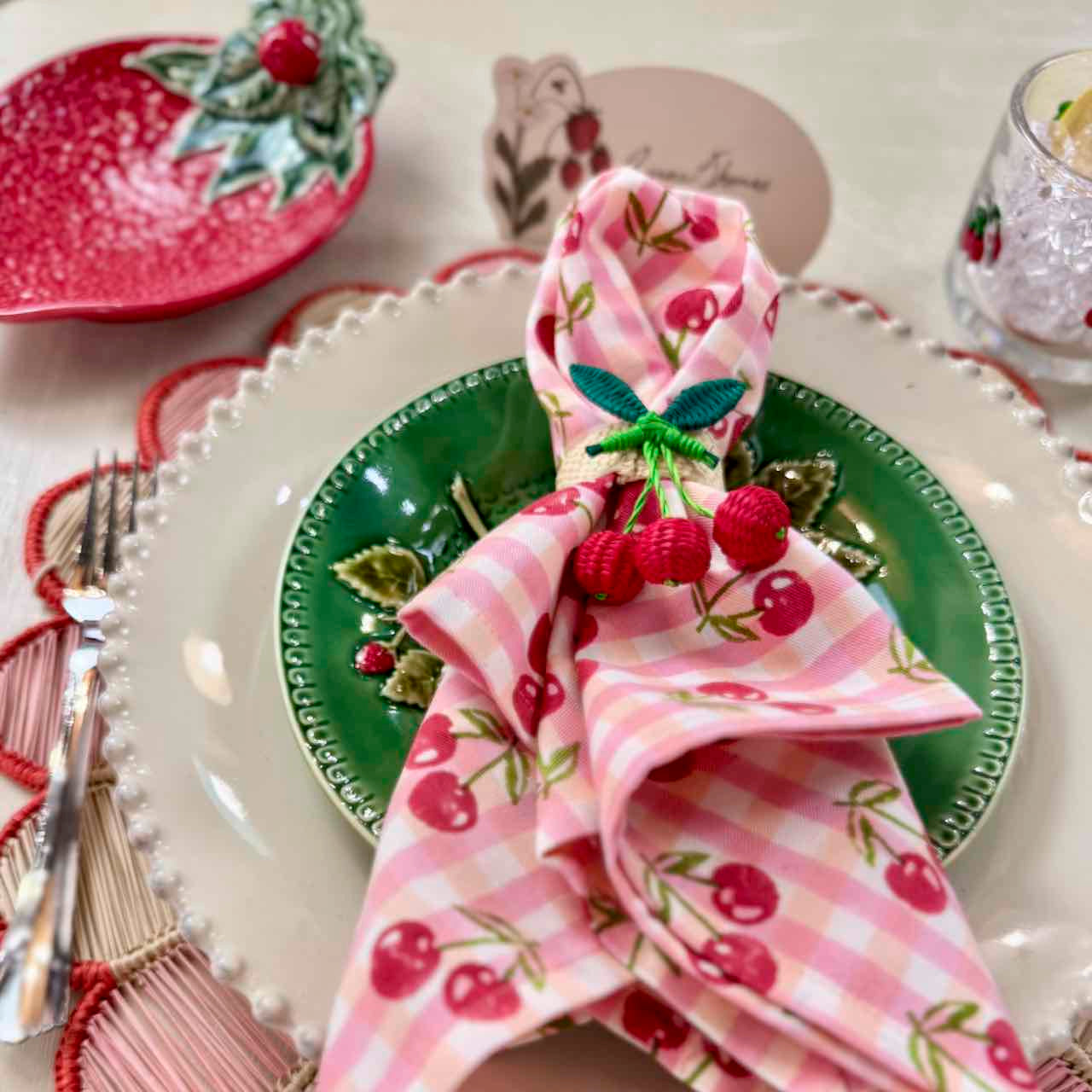 Decorative table setting with a pink cherry-themed napkin on a green plate.