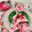 Decorative table setting with a pink cherry-themed napkin on a green plate.