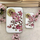 Two phone cases with floral design on a marble surface with flowers around