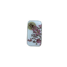 A small rectangular white tin with a floral print of pink blossoms and brown leaves, resting on a light-colored wooden surface.