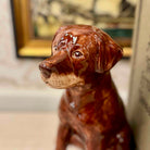 Brown ceramic dog figurine in a room with a blurred painting in the background