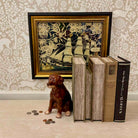 Decorative setting with a framed artwork, books, and a dog figurine on a patterned wall background.