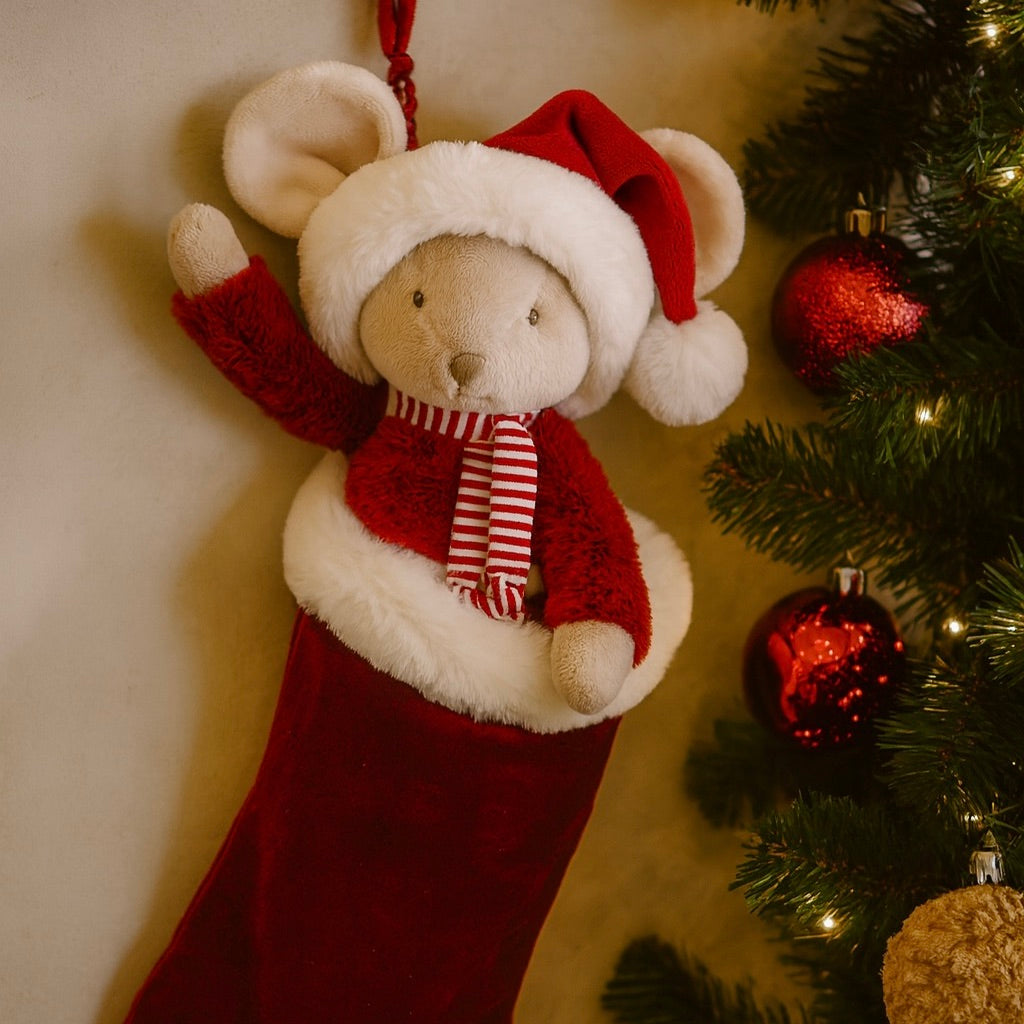Plush bear in a red and white outfit with a Santa hat, scarf, and mittens hanging from a Christmas tree.