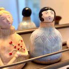 Two ceramic figurines with decorative clothing and accessories on a reflective surface.