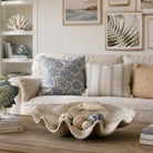 A styled living room scene featuring a cream sofa with decorative throw pillows, a wooden coffee table with a large clam shell bowl, and framed wall art in a bright, neutral interior.