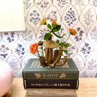 Decorative arrangement of mushrooms and flowers on a book with a floral-patterned wallpaper background.