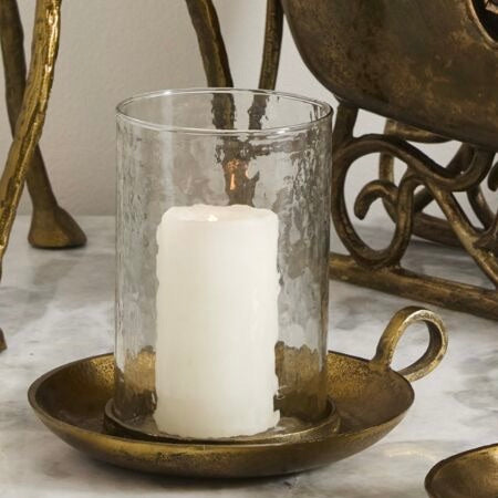 White candle in a glass holder on a bronze tray with decorative background