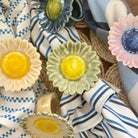 Decorative ceramic sunflower napkin rings on a variety of fabric backgrounds.