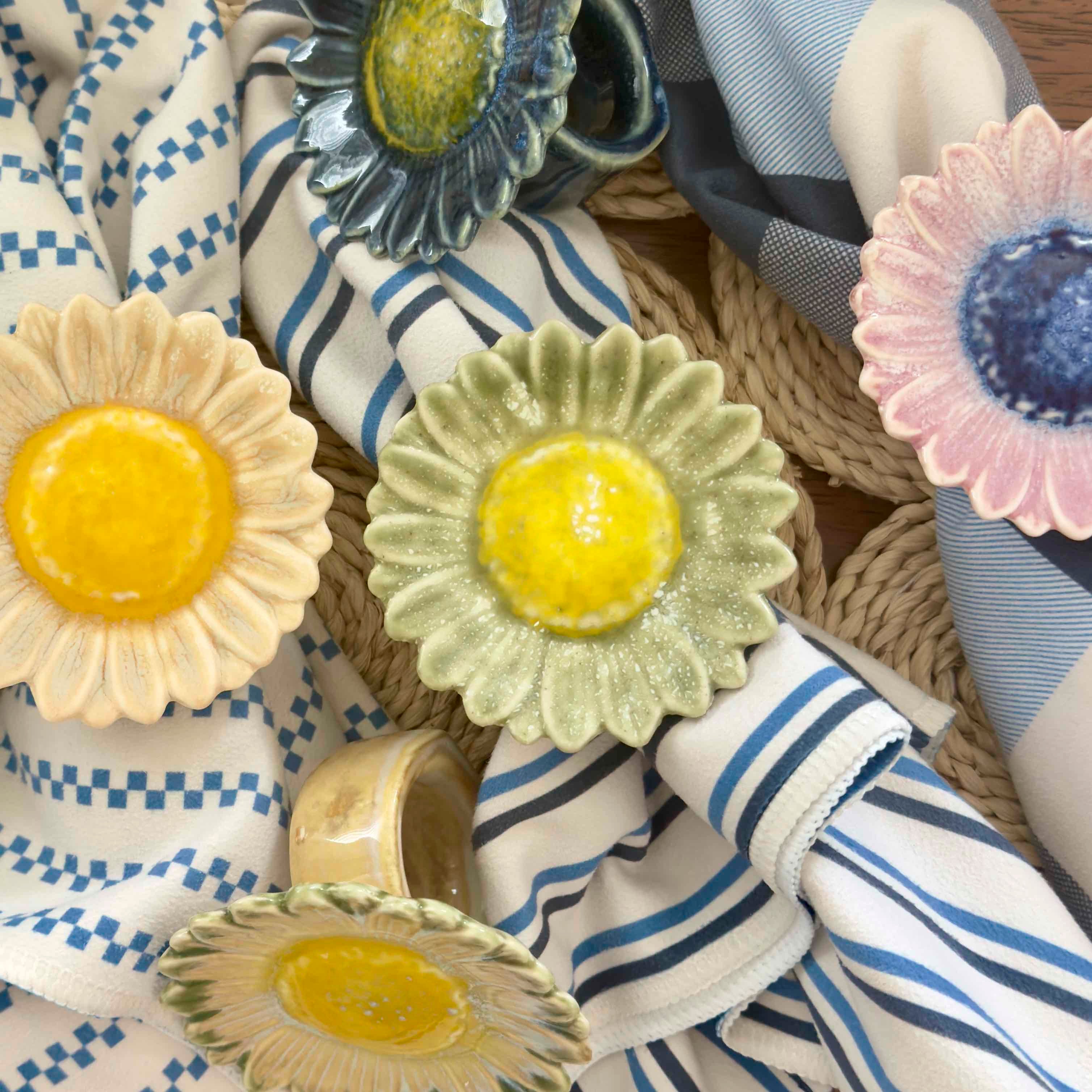 Decorative ceramic sunflower napkin rings on a variety of fabric backgrounds.