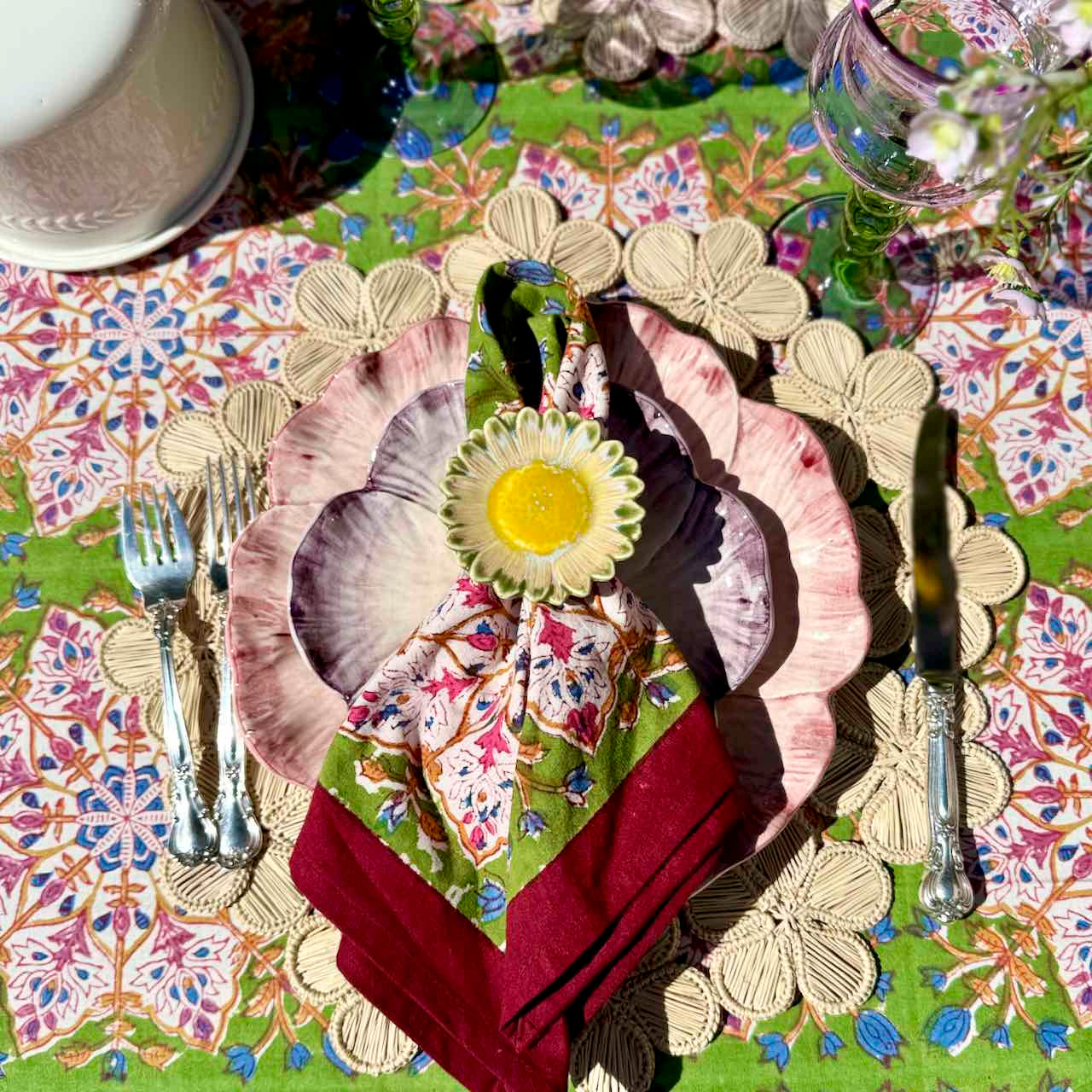 Decorative table setting with floral plates, napkin, and cutlery on a patterned tablecloth.