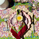 Decorative table setting with floral plates, napkin, and cutlery on a patterned tablecloth.