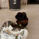 Decorative item with a metallic heart and black rose on a textured surface