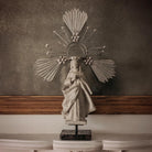 Statue of a woman with a sun-like headdress on a marble surface against a textured wall.