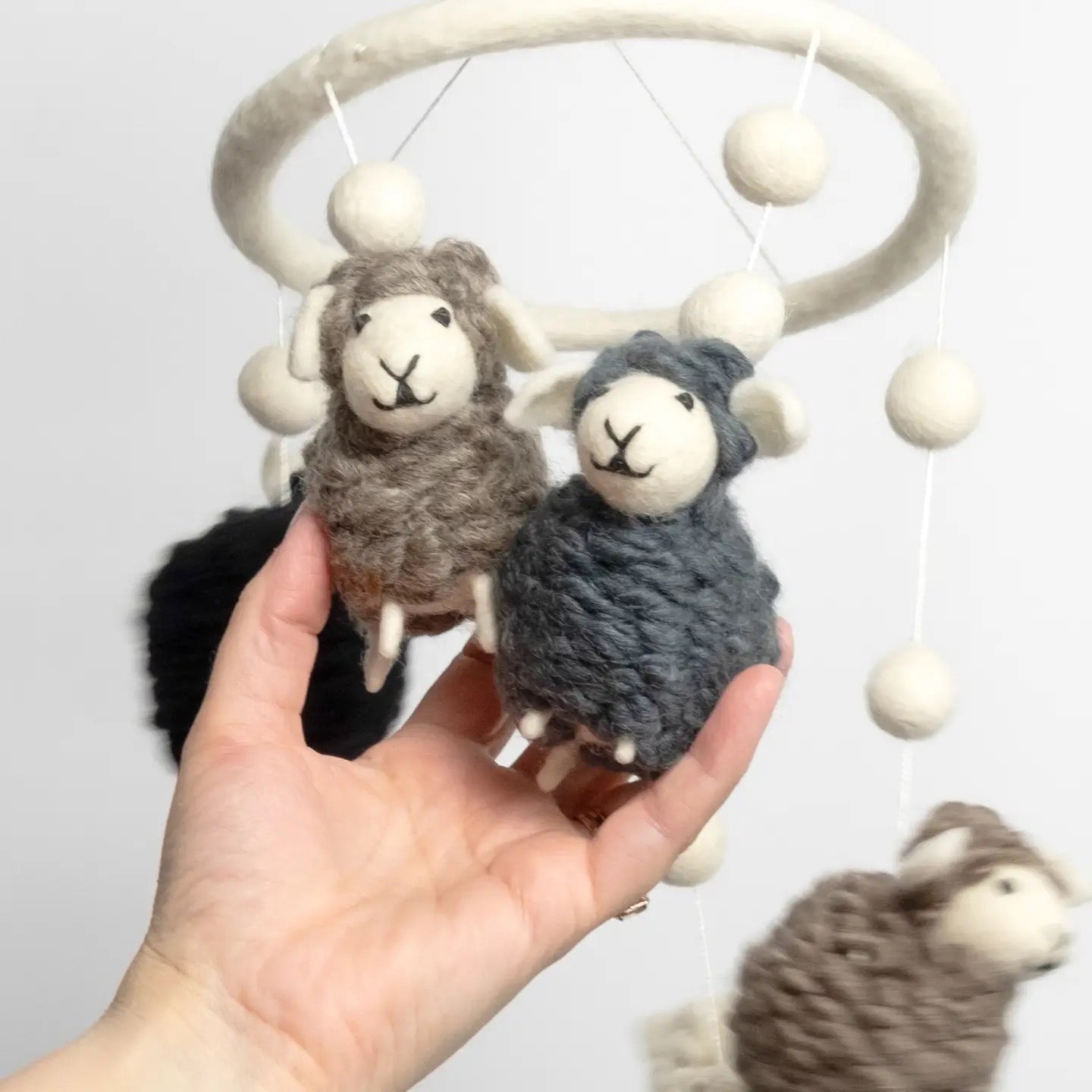 Hand holding a small sheep toy with a larger sheep toy and white beads in the background.