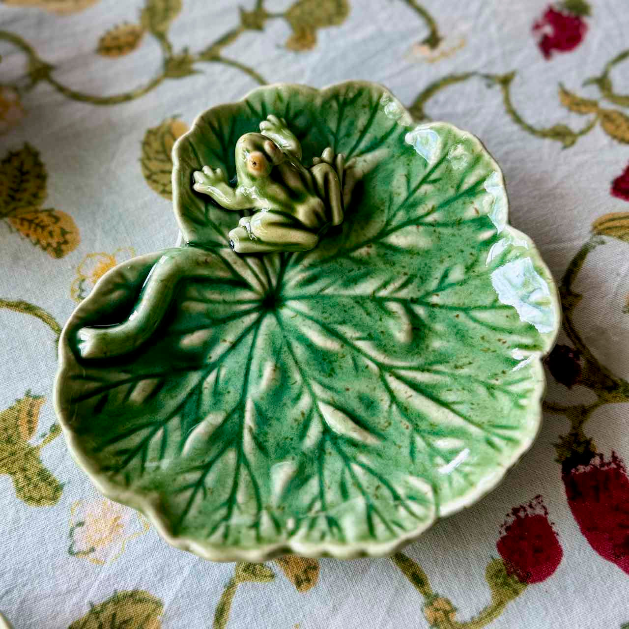 Green ceramic leaf-shaped dish with a frog on a floral-patterned fabric background