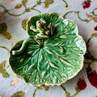 Green ceramic leaf-shaped dish with a frog on a floral-patterned fabric background