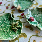 Ceramic leaf-shaped dishes with a ladybug and frog on a floral-patterned surface