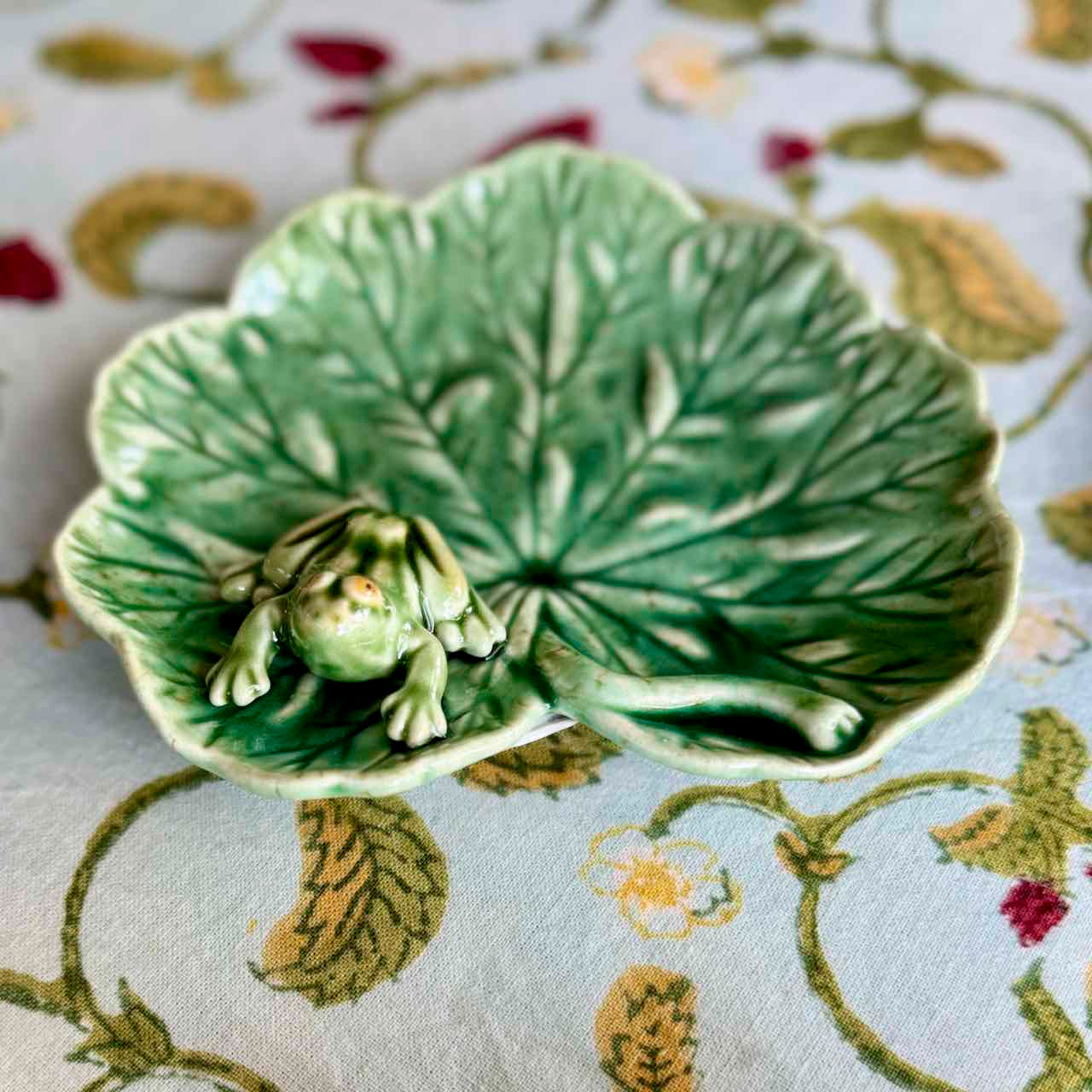 Green ceramic leaf-shaped dish with a frog on a floral-patterned fabric background