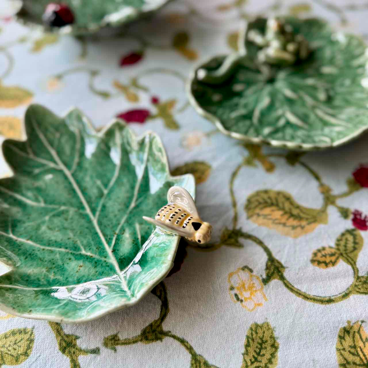 Green ceramic leaf-shaped dish with a small gold turtle on a floral-patterned fabric background