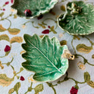 Green leaf-shaped ceramic dish with a gold ring on a floral-patterned fabric background