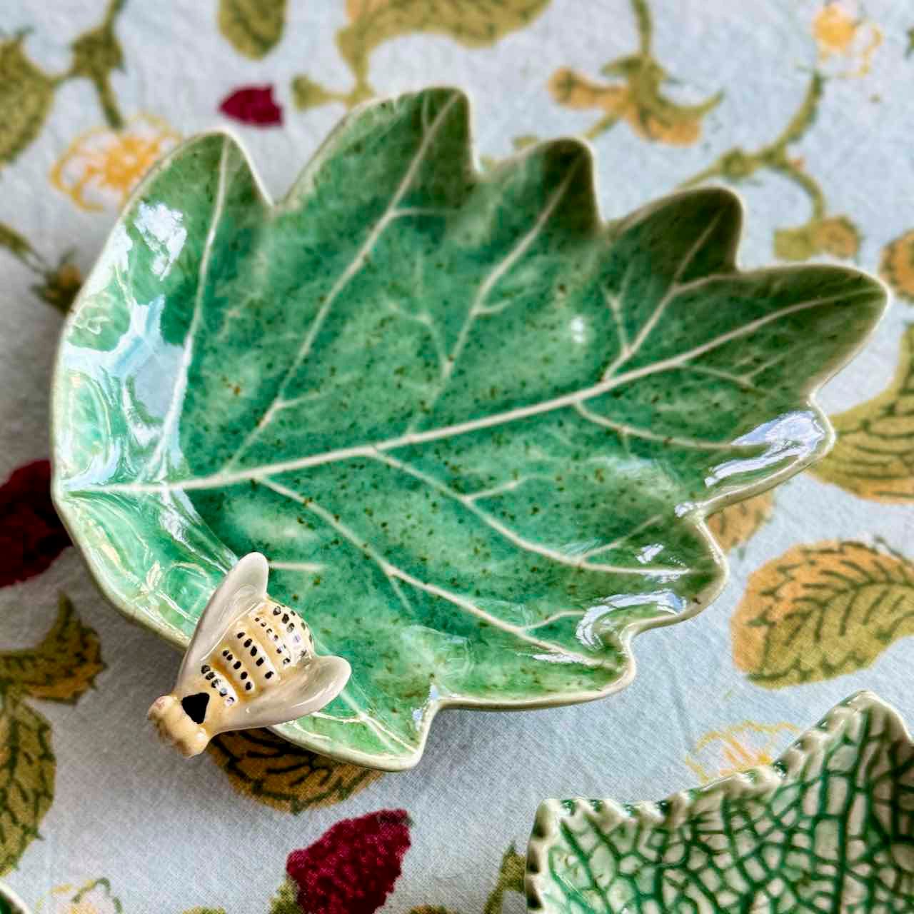Green leaf-shaped ceramic dish with a bee figurine on a floral tablecloth
