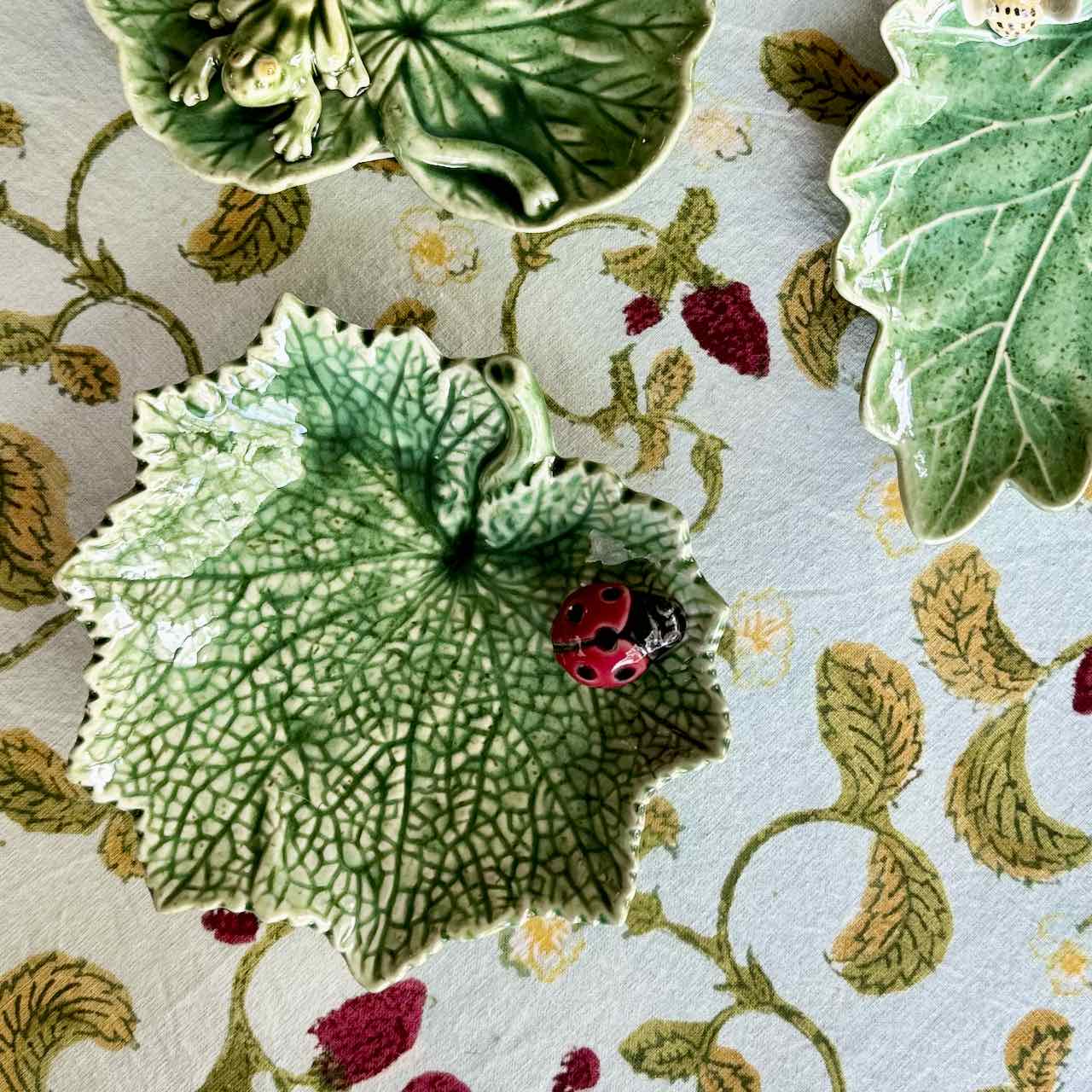 Decorative ceramic tiles with leaf and ladybug designs on a floral-patterned surface.