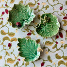 Three green ceramic leaf-shaped dishes on a decorative fabric background