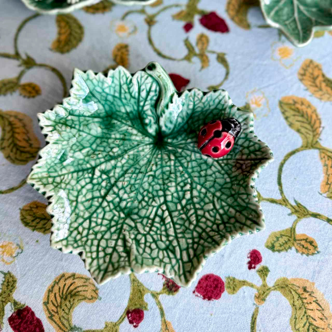 Decorative ceramic leaf with a ladybug on a floral-patterned fabric background
