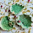 Three green leaf-shaped ceramic dishes on a floral-patterned fabric background