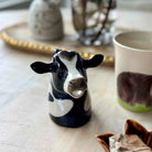 Ceramic cow figurine on a table with a mug featuring a cow design.