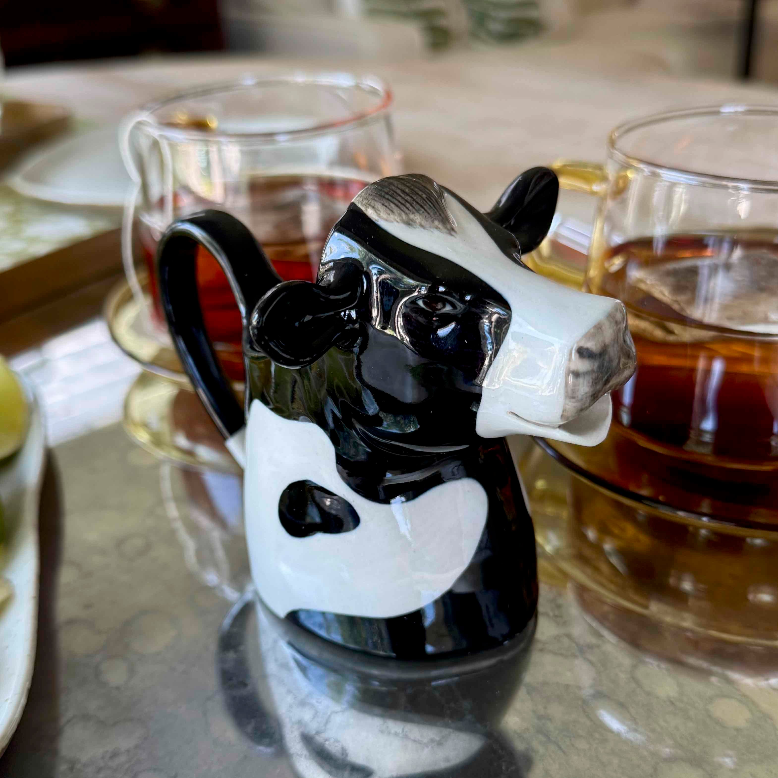 Cow-shaped mug on a reflective surface with cups in the background
