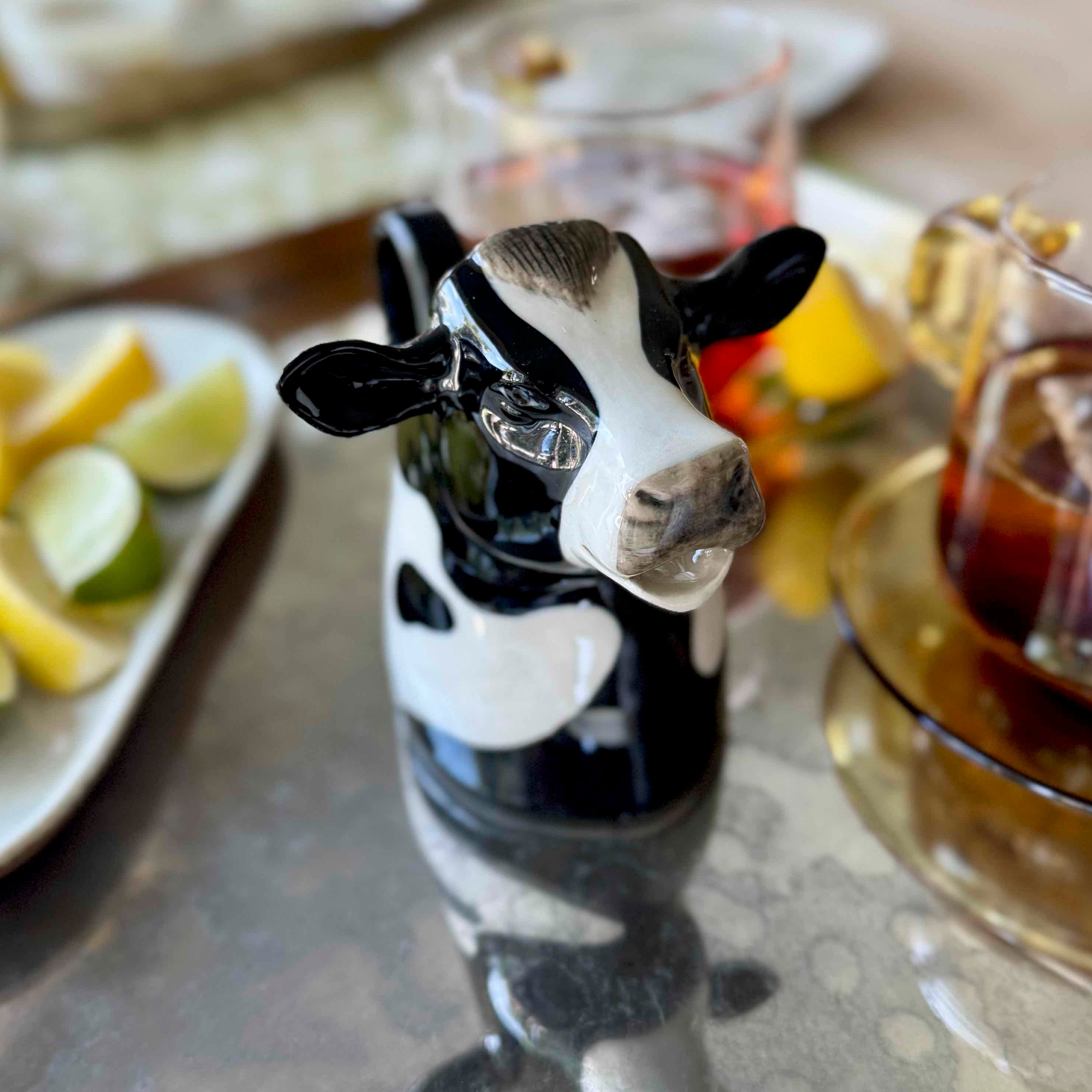 Cow-shaped bottle stopper on a table with drinks and fruit in the background